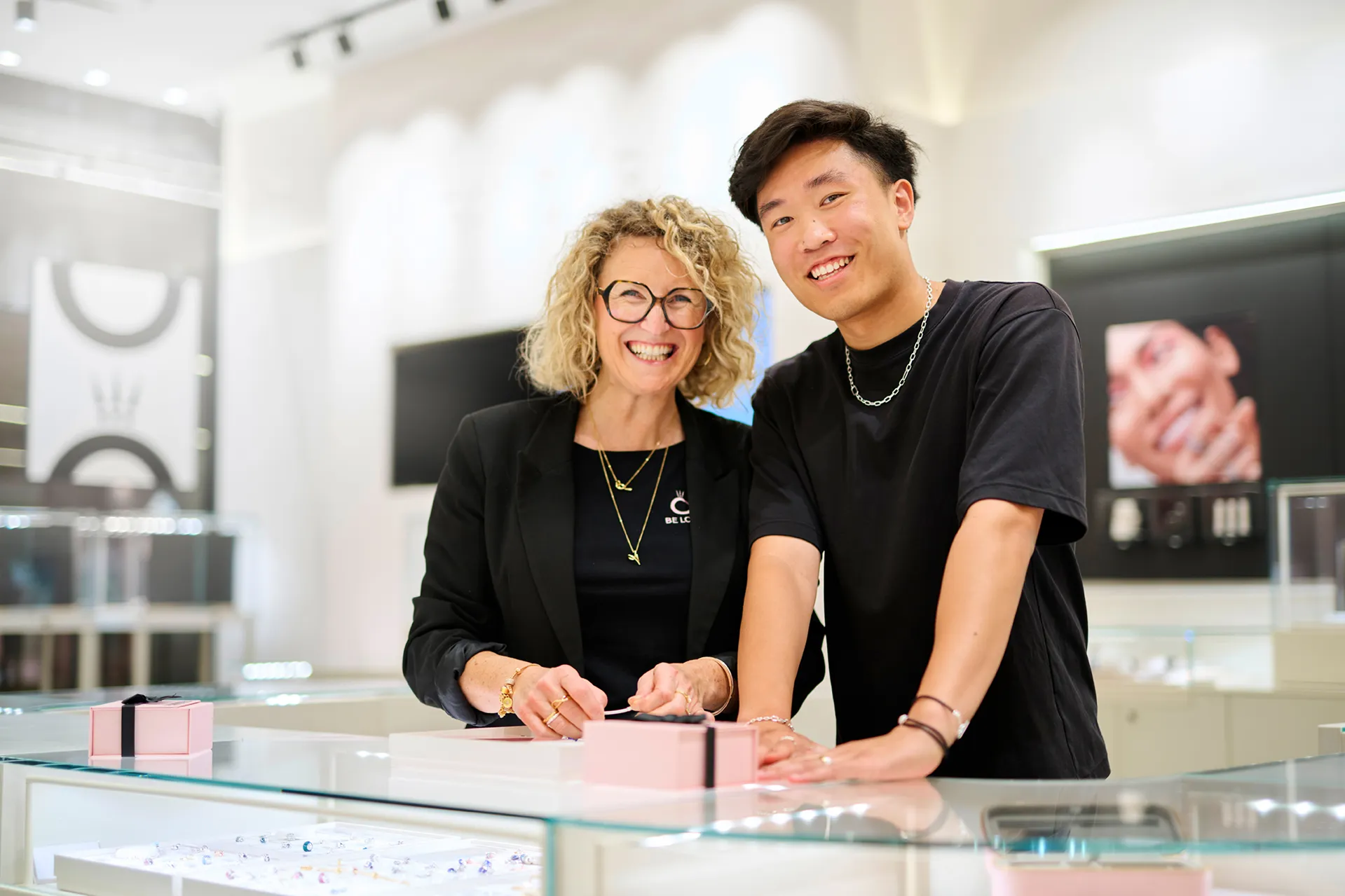 Jewelry store staff smiling and assisting a customer with a bracelet at a counter