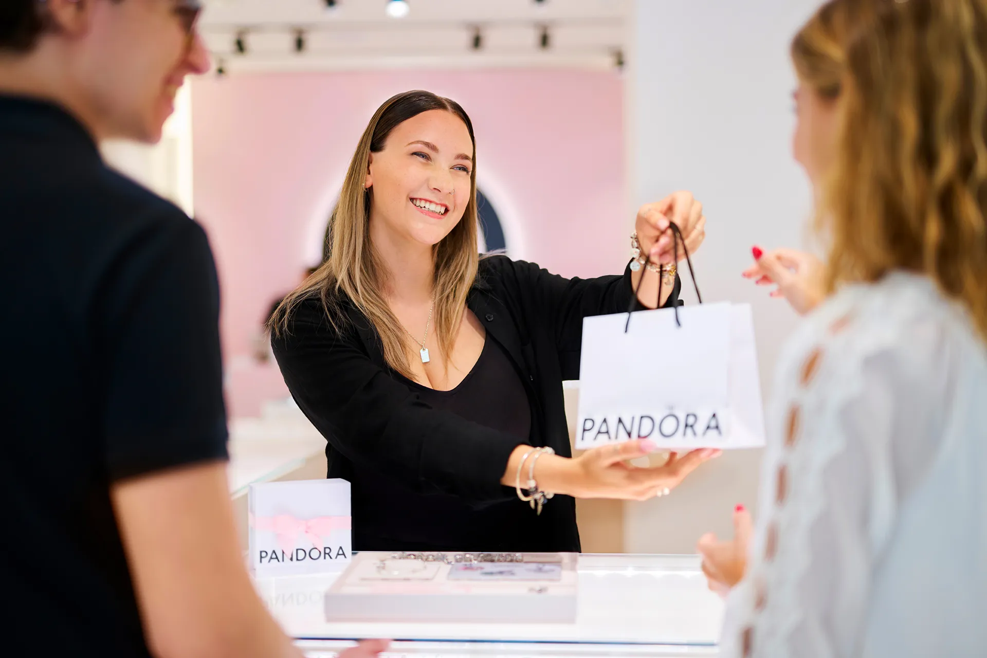 Jewelry store staff smiling and assisting a customer with a bracelet at a counter