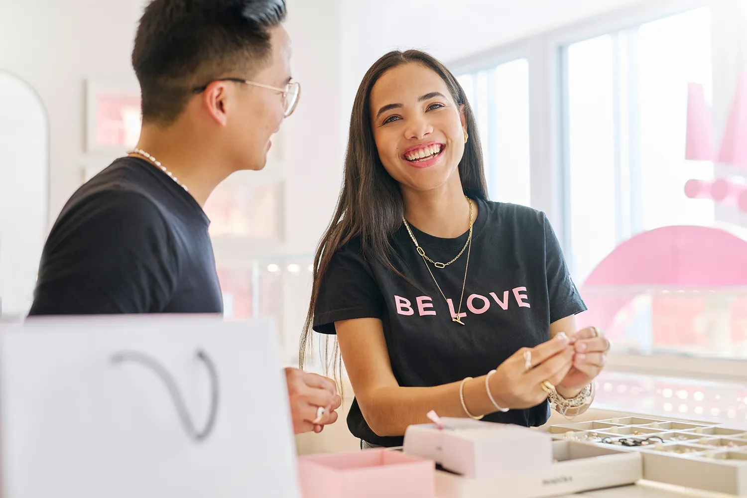 Jewelry store staff smiling and assisting a customer with a bracelet at a counter