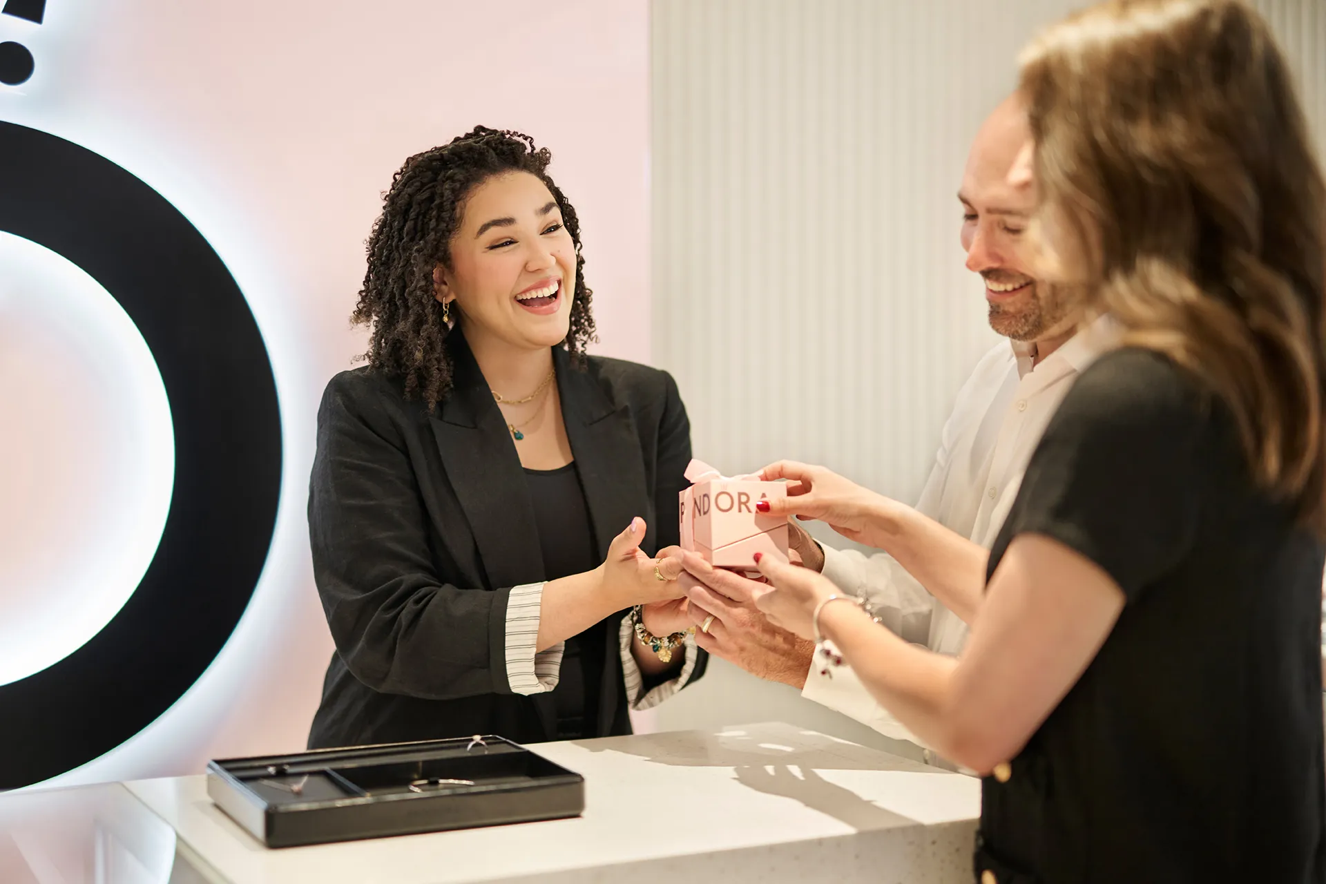Jewelry store staff smiling and assisting a customer with a bracelet at a counter